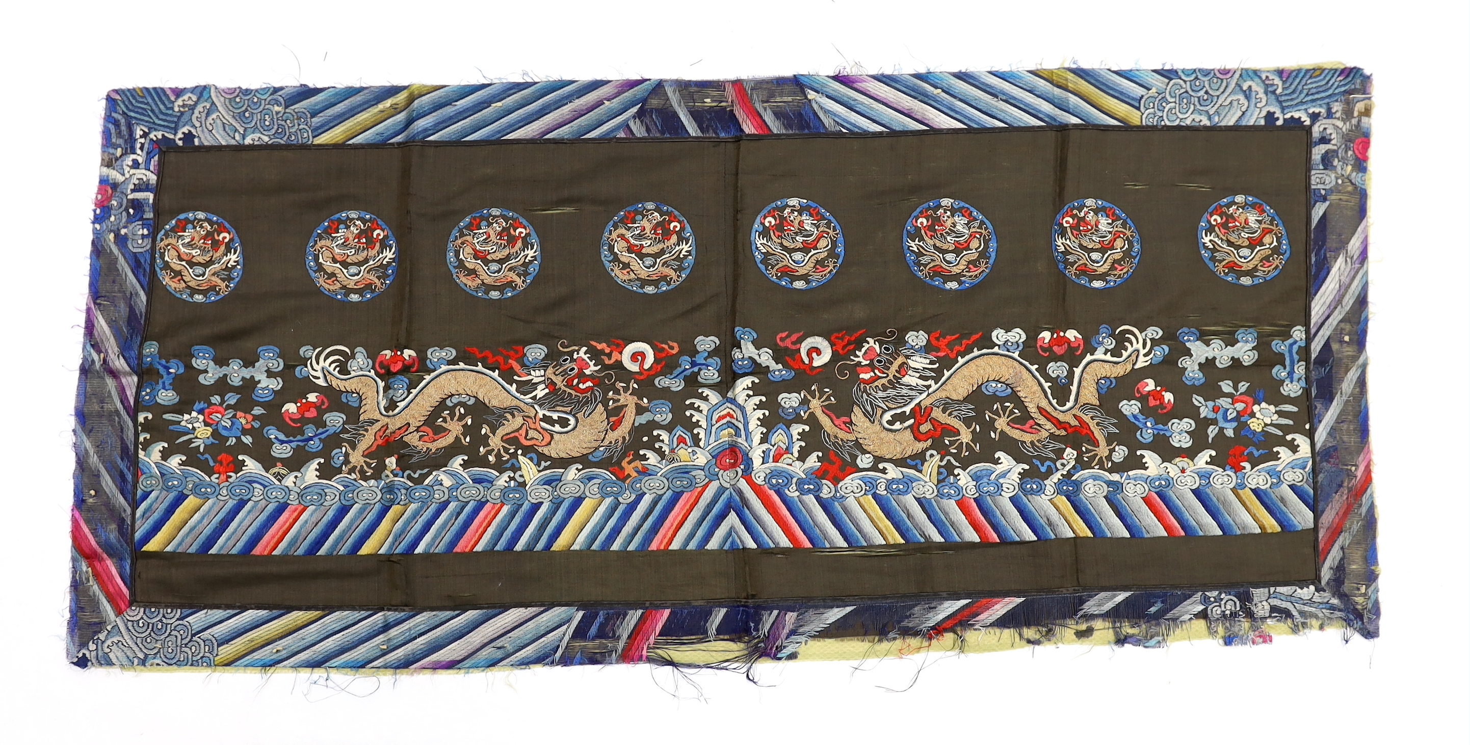 A Chinese polychrome silk and gold thread embroidery on a black silk background, possibly from the lower section of a robe, depicting dragons and auspicious symbolic motifs, 130cm long x 59cm high